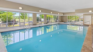 Una amplia piscina interior con ventanas de vidrio transparente, una silla de salvavidas y una parrilla afuera.