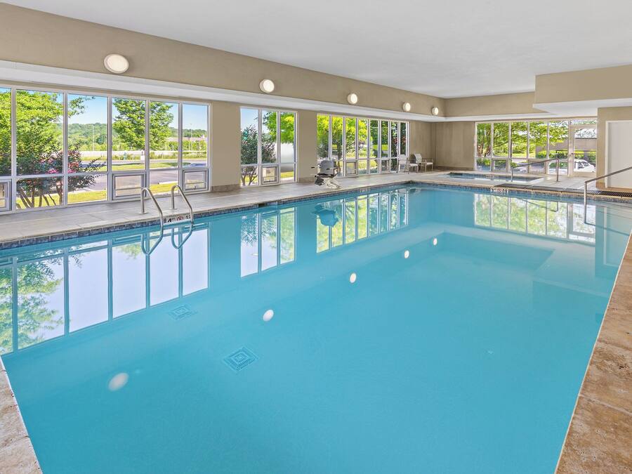 Una amplia piscina interior con ventanas de vidrio transparente, una silla de salvavidas y una parrilla afuera.