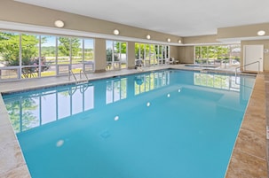 Uma grande piscina interior com janelas de vidro transparente, uma cadeira de salva-vidas e uma churrasqueira lá fora.