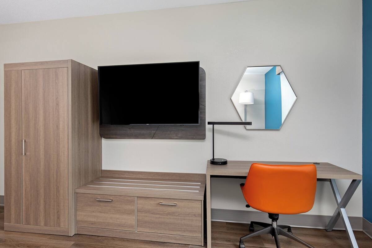 Une chambre à coucher comprenant un lit, une armoire, un bureau, une chaise, une télévision et un miroir.