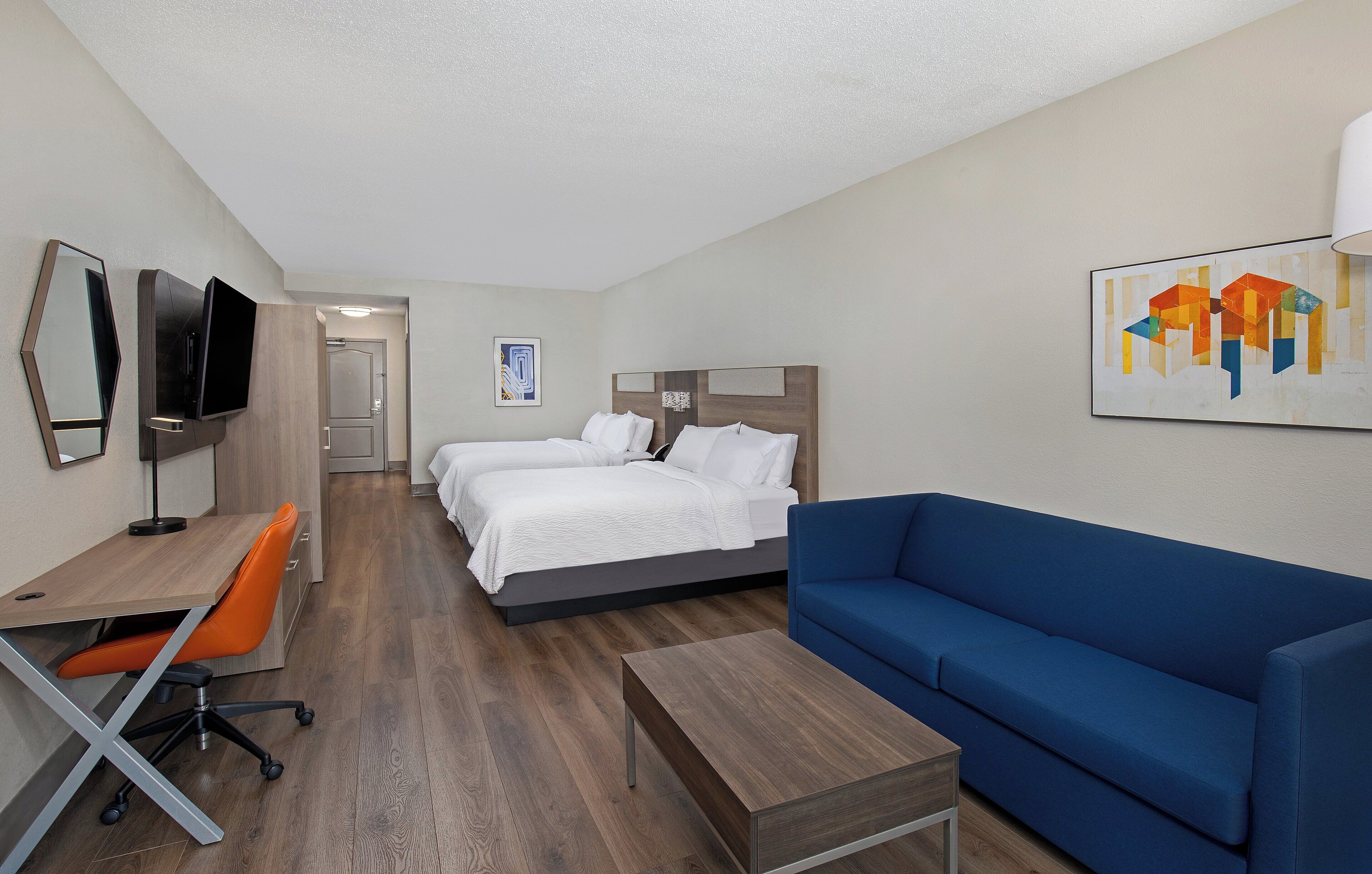 Een hotelkamer met een bed, een blauwe bank, een bureau met een oranje fauteuil en een aan de muur bevestigde televisie.