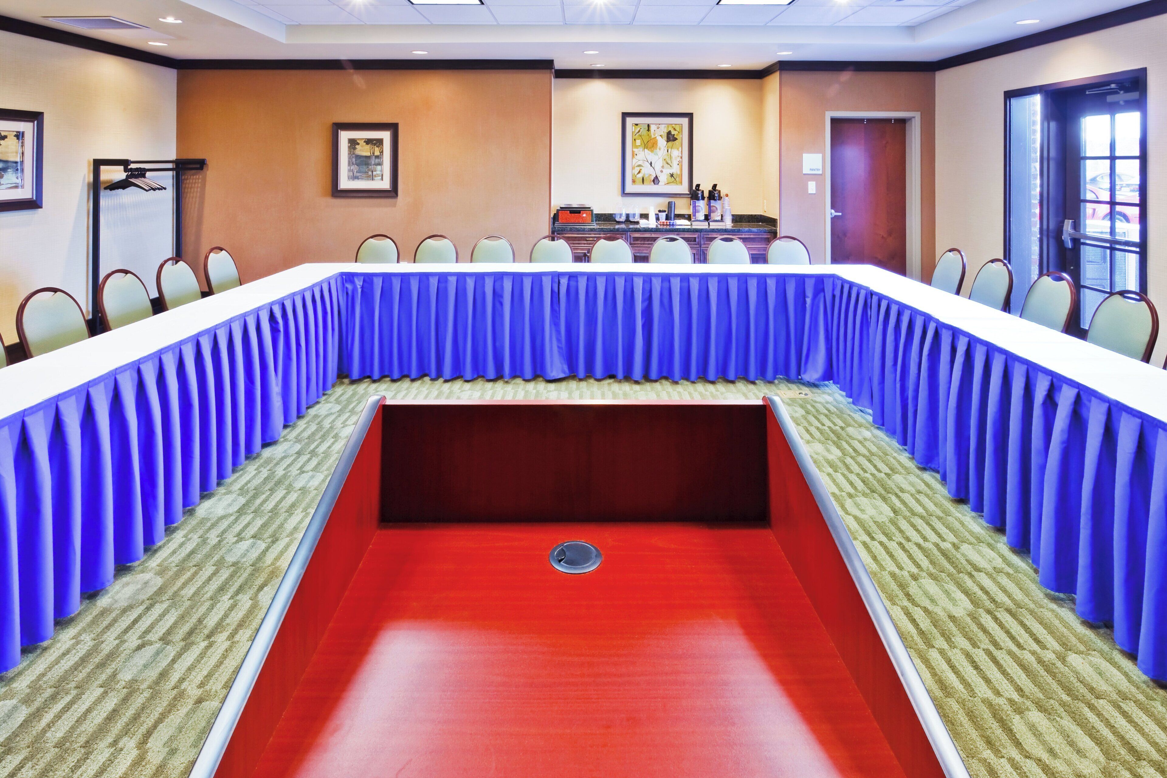 Sala de conferência com uma mesa comprida, cadeiras, um púlpito e um espaço para buffet.