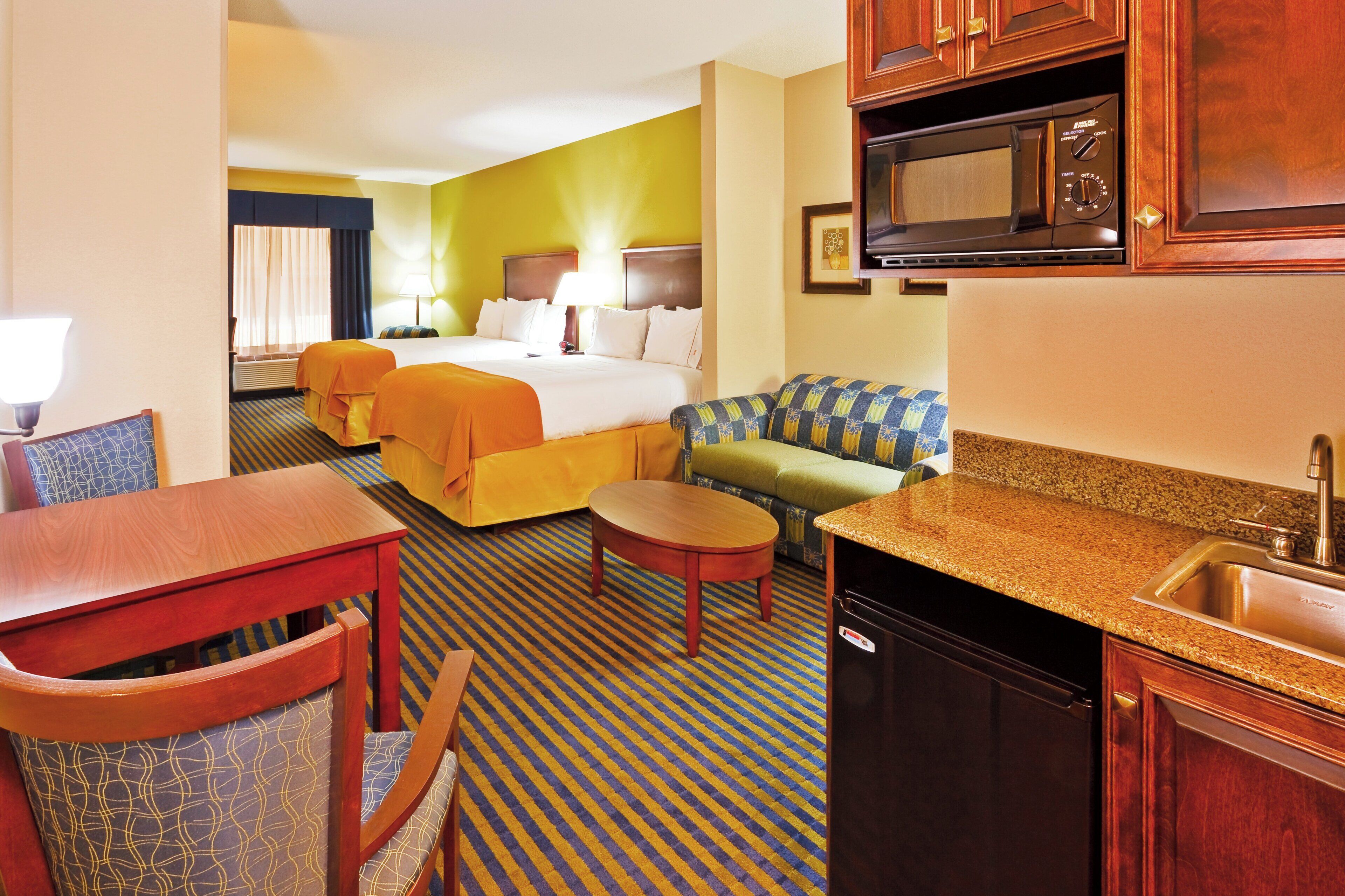Habitación de hotel con cama, sofá, mesa de comedor y cocina equipada con microondas y lavaplatos.