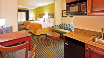 A hotel room with a bed, a sofa, a dining table, a kitchen area with a microwave, and a sink.