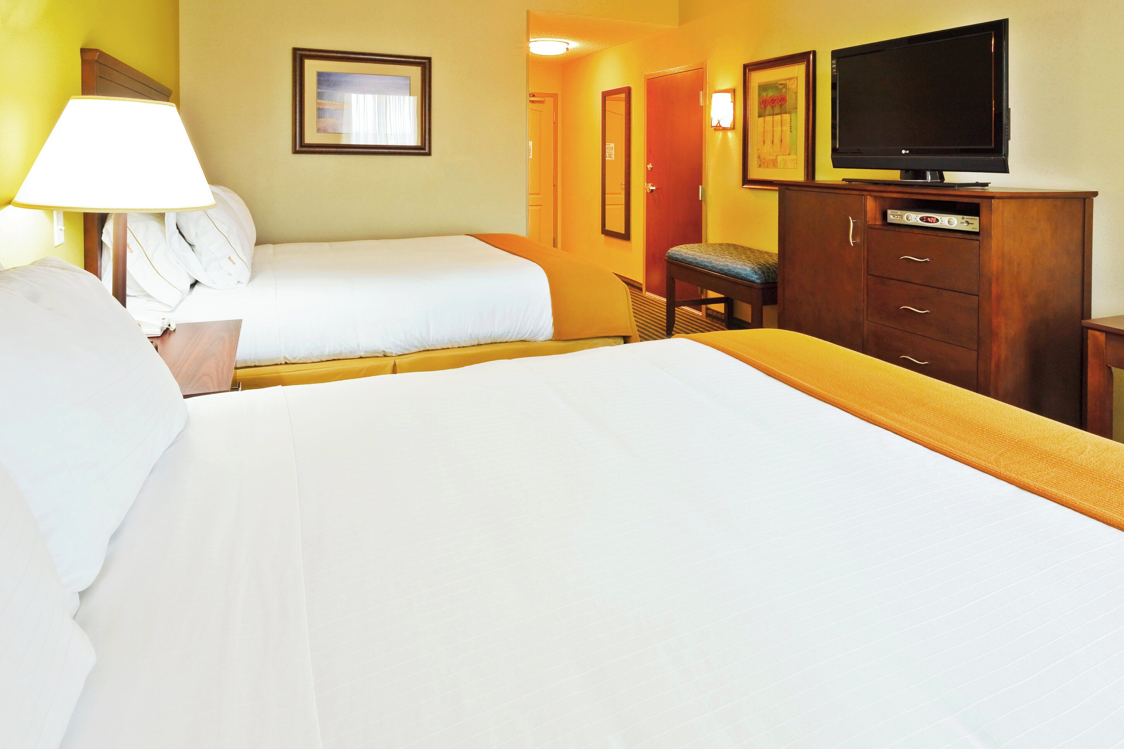 A hotel room with two beds, a television, a desk, and a chair.