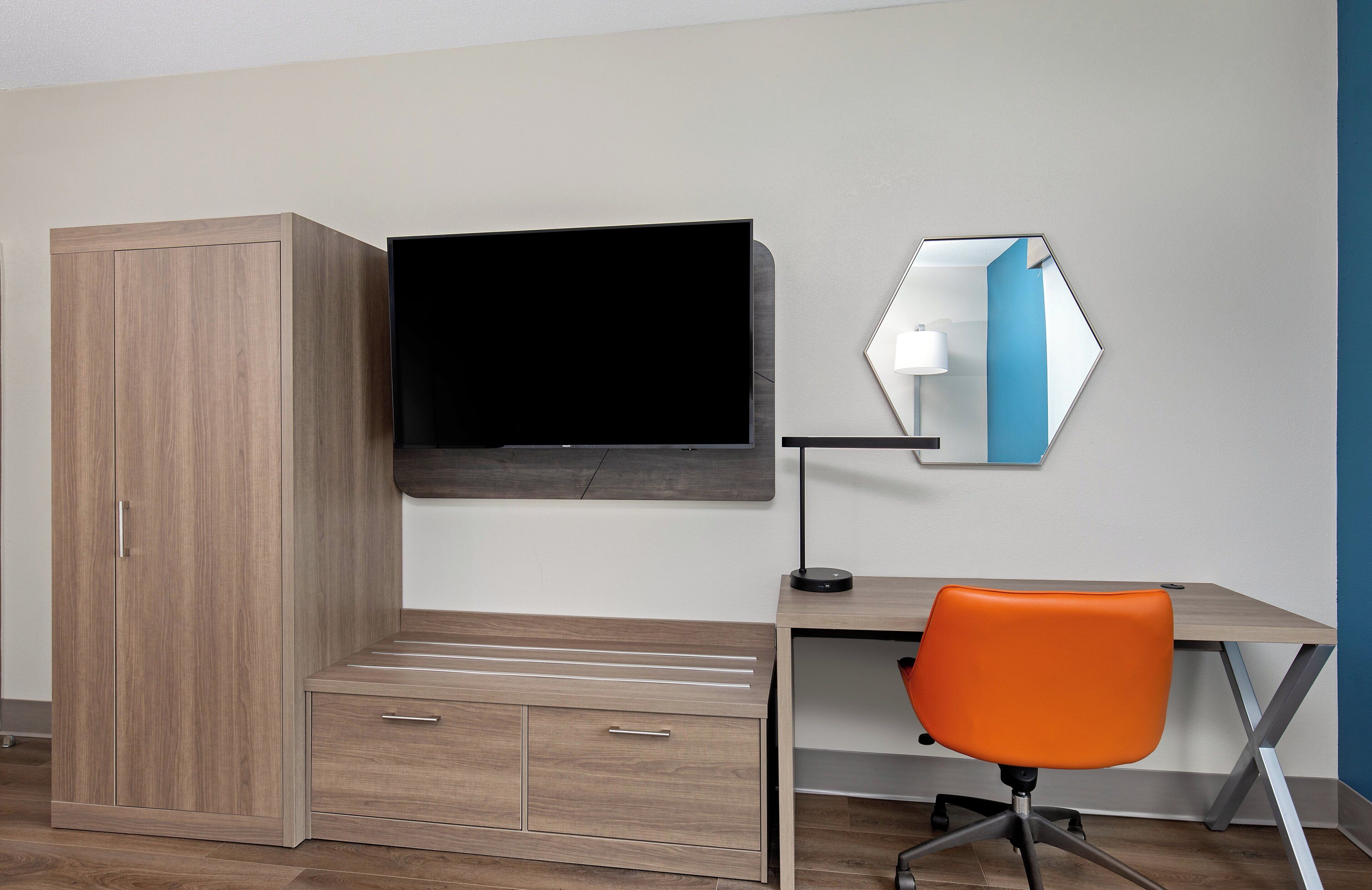 Ein Zimmer mit Holzschrank, Schreibtisch mit Stuhl, Flachbildfernseher und Spiegel.