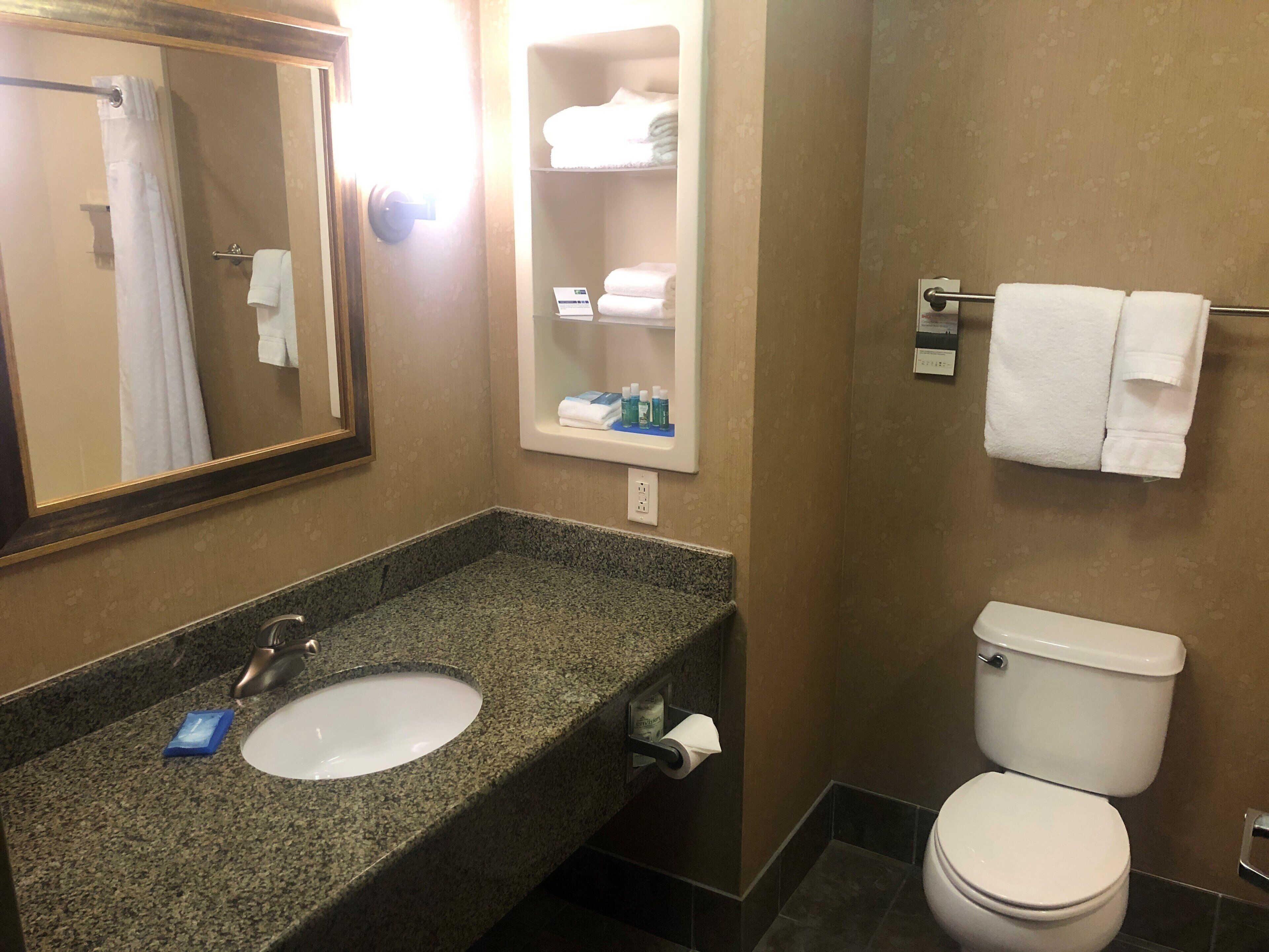 Un baño con lavamanos de encimera de granito, un espejo, toallero y un inodoro.