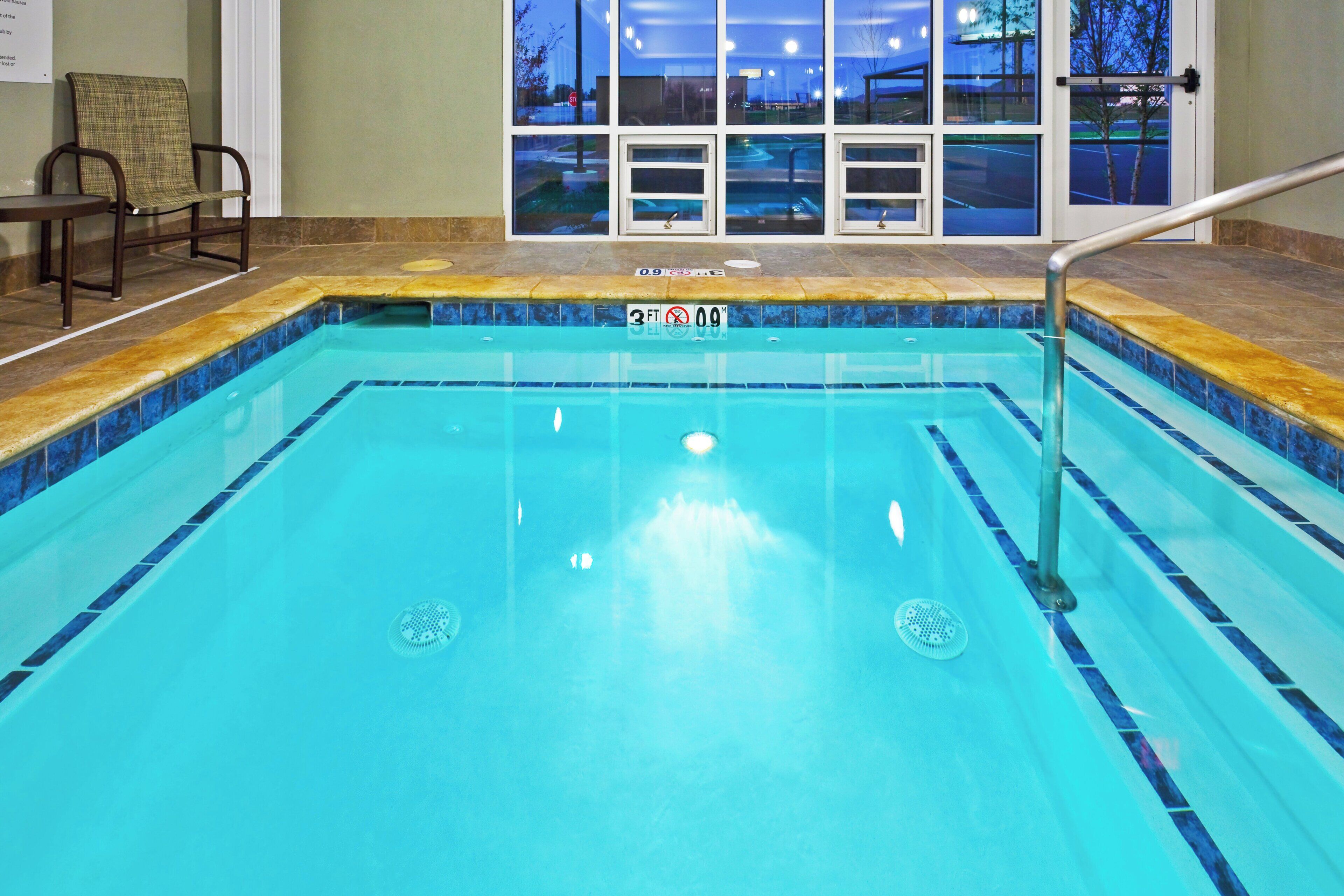 An indoor swimming pool with clear water, a safety sign, and a view of the outside through large windows.