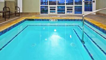An indoor swimming pool with clear water, a safety sign, and a view of the outside through large windows.