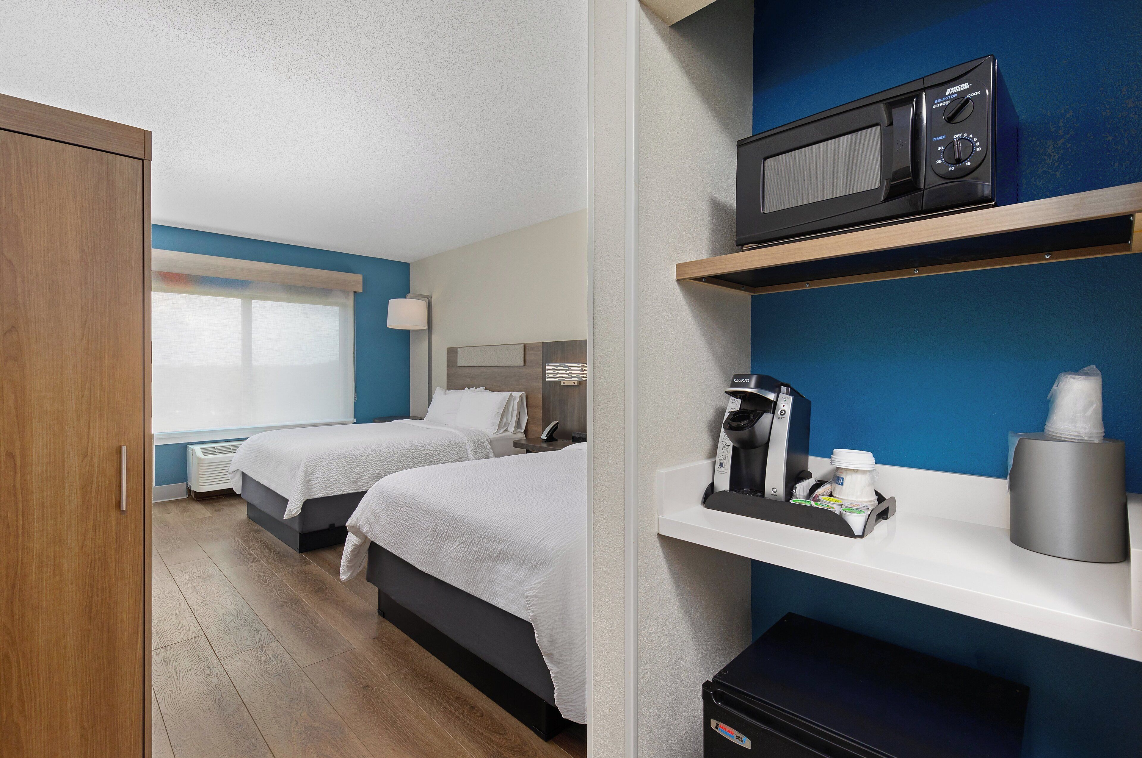 A hotel room with two beds, a microwave on a shelf, a coffee maker, and a tissue dispenser.