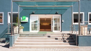 L’entrée d’un hôtel Holiday Inn, avec une façade en verre, un auvent vert et un escalier menant à l’entrée.