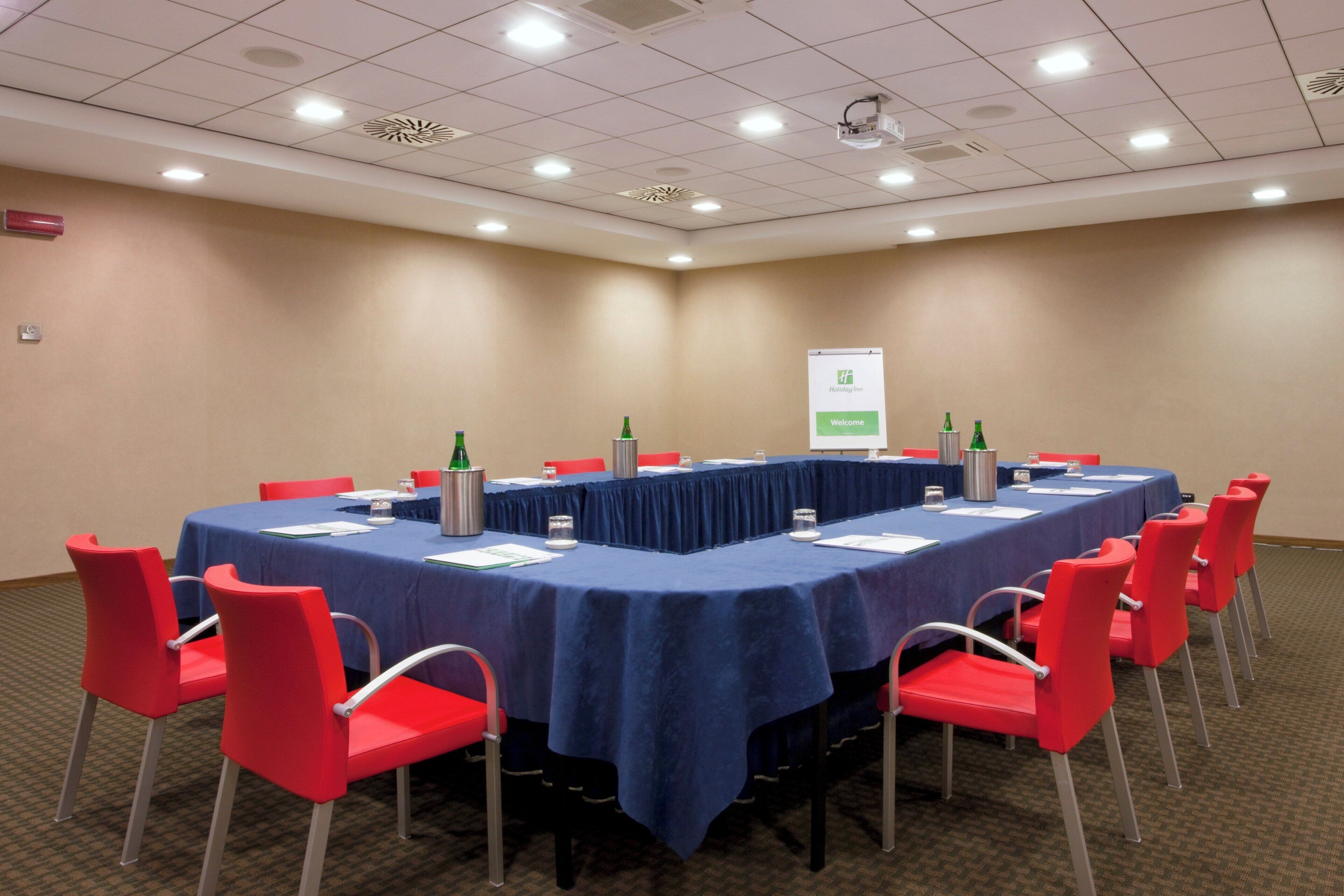Un salón de conferencias con una mesa larga, sillas rojas y un cartel en la pared.