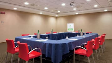 Un salón de conferencias con una mesa larga, sillas rojas y un cartel en la pared.