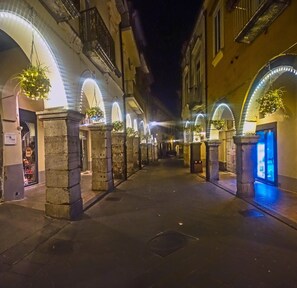 Un carrer nocturn amb edificis d'arcs, il·luminat per llums de garlandes i plantes penjants.