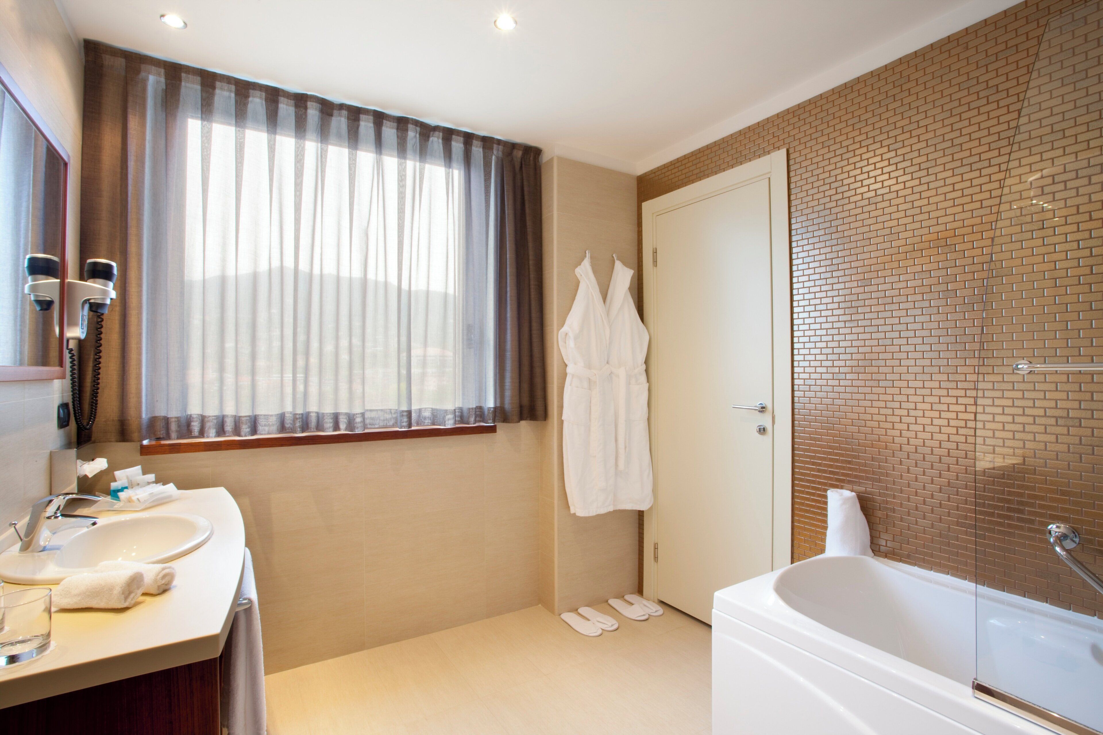 A bathroom with a bathtub, a sink, a mirror, a window with curtains, and a towel rack.