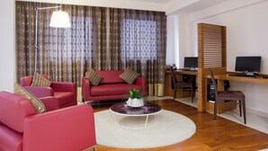 Un salon moderne avec un canapé rouge, une table basse, un bureau avec un ordinateur et une grande fenêtre avec des rideaux.