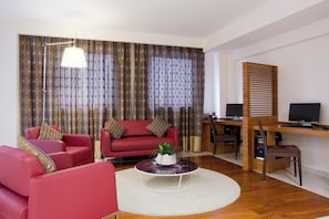 Una sala de estar moderna con un sofá rojo, una mesa de centro, un escritorio con una computadora y un ventanal con cortinas.