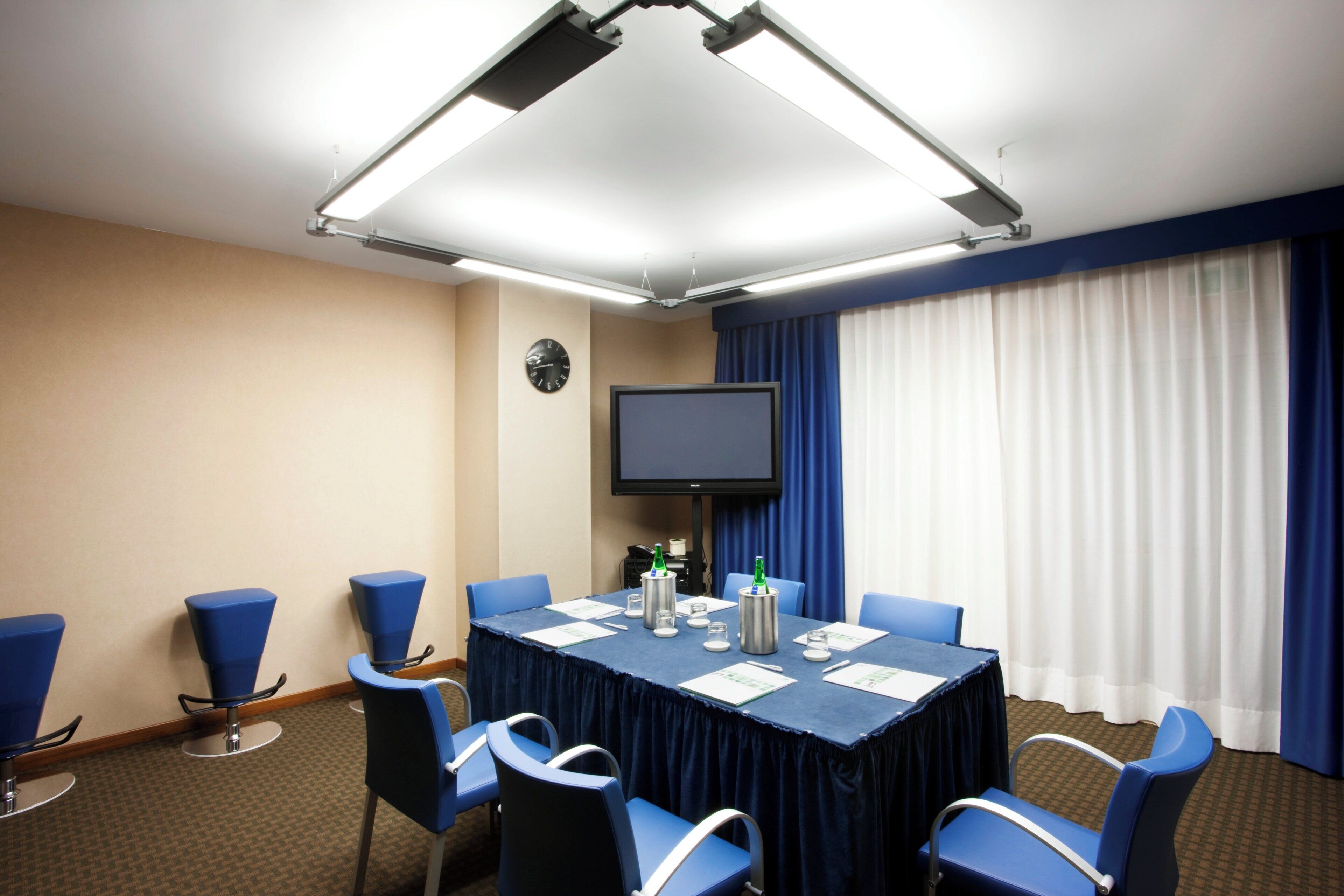 A conference room with a table, chairs, a clock, and a television.