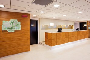 Un comptoir d’accueil avec un revêtement en bois, une enseigne indiquant qu’il s’agit d’un hôtel de la chaîne Holiday Inn, et un plafond carrelé doté d’un éclairage encastré.