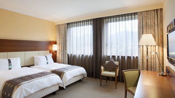 Una habitación de hotel con dos camas, un escritorio, una silla, un televisor y cortinas.