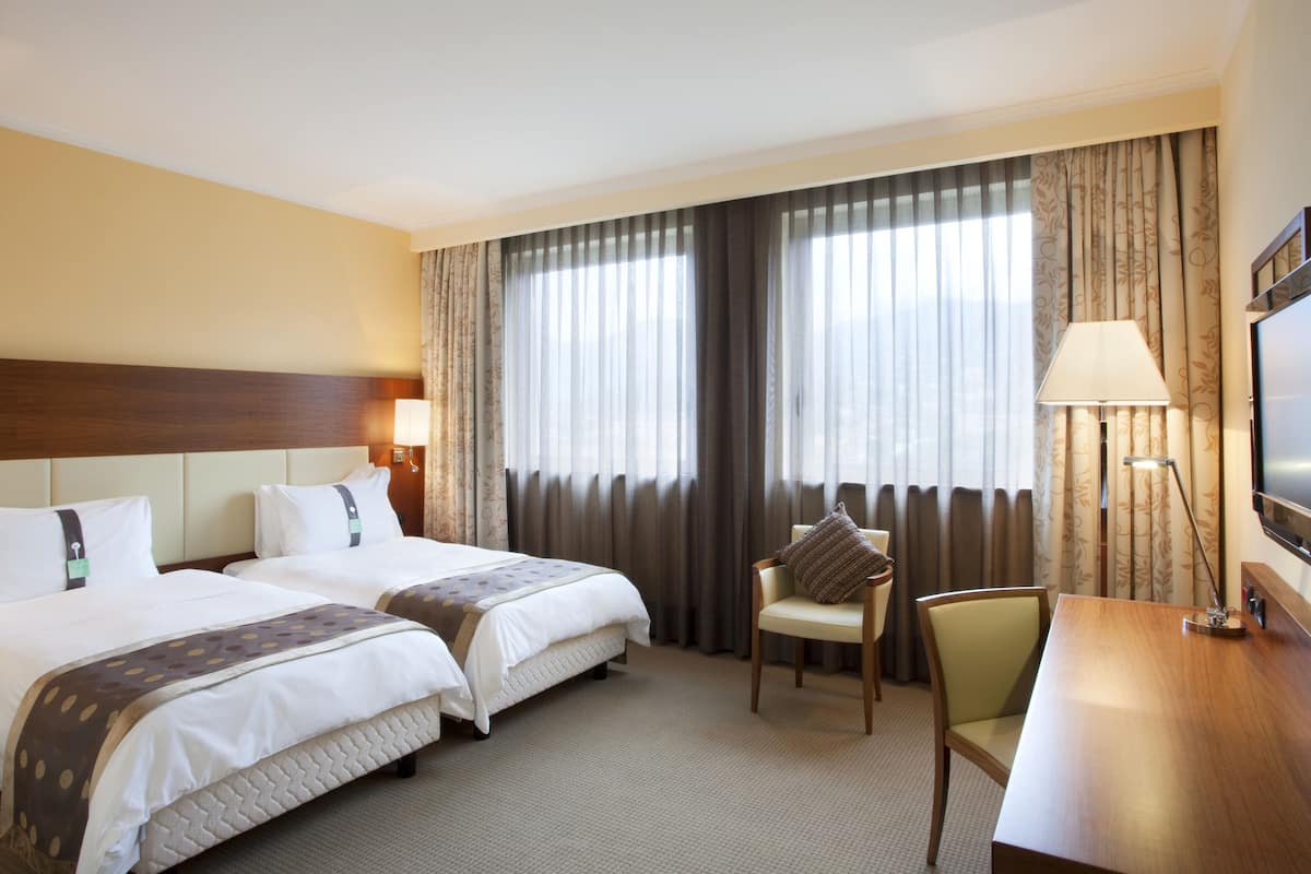 Una habitación de hotel con dos camas, un escritorio, una silla, un televisor y cortinas.