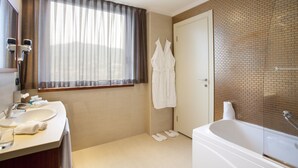 Un baño moderno con una bañera grande, un tocador con lavabo y una ventana con cortinas traslúcidas.