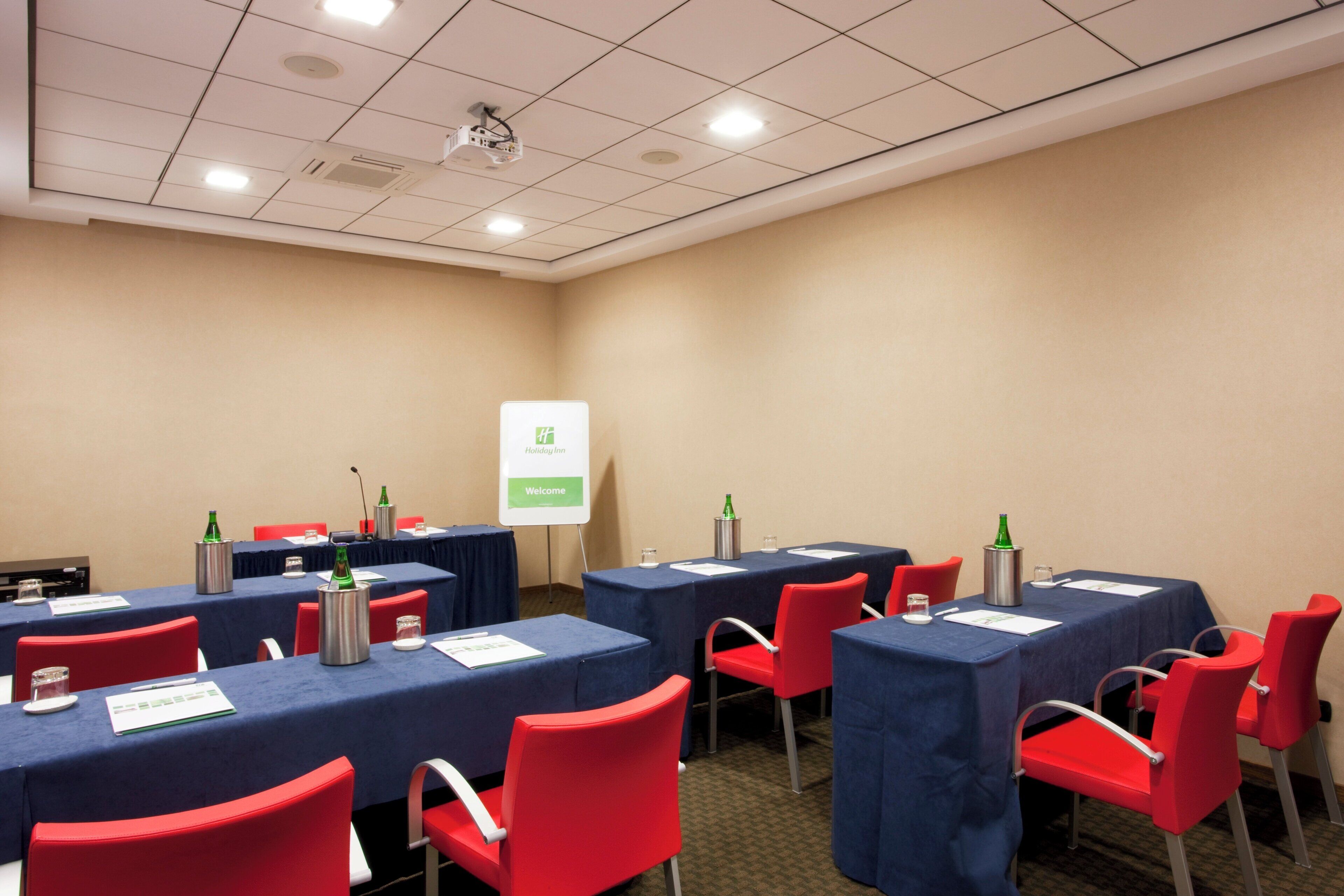 Uma sala de conferências com mesas, cadeiras e uma tela de projeção.