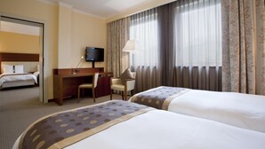 Una habitación de hotel con dos camas, un escritorio con silla, una televisión y una ventana con cortinas.