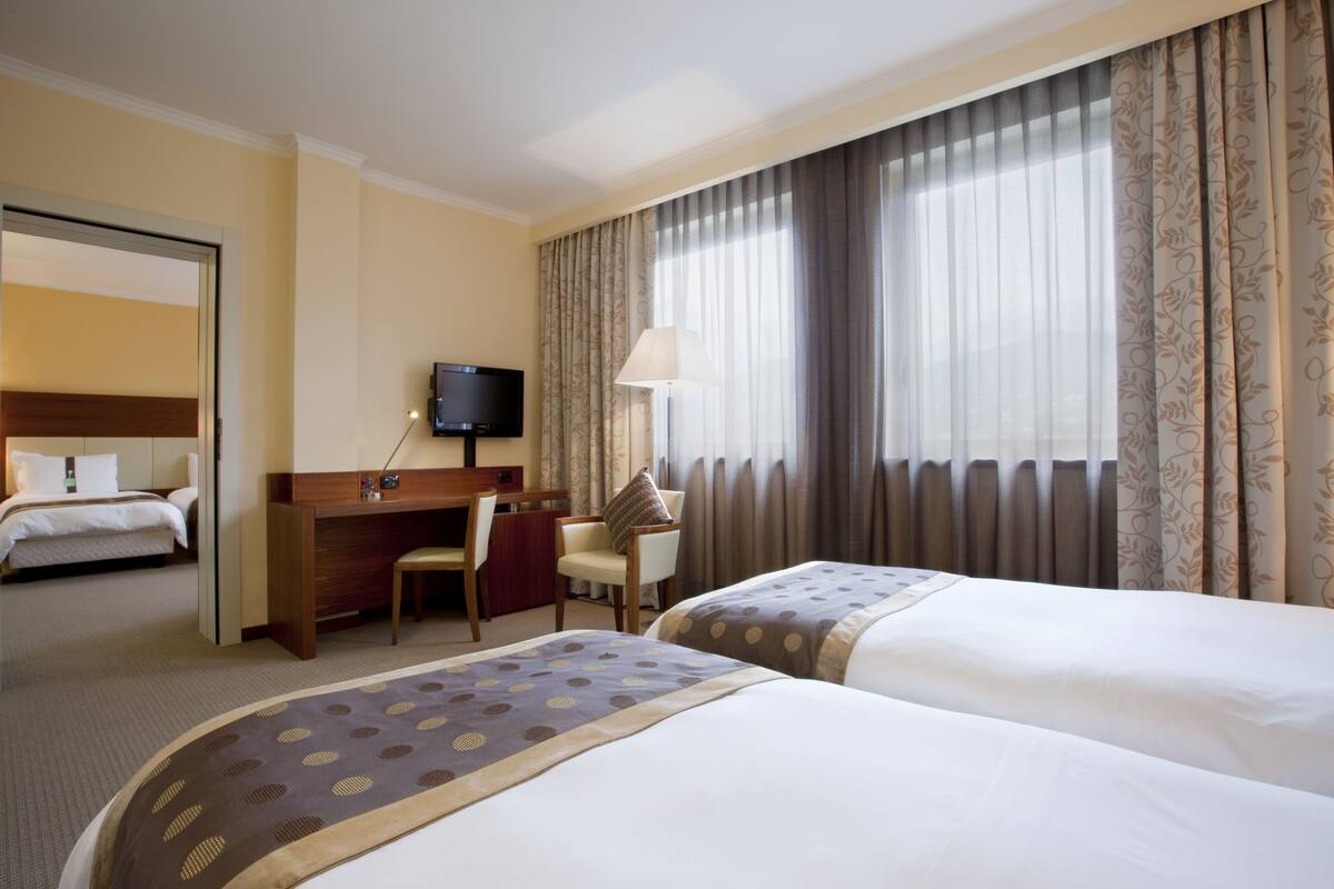 Una habitación de hotel con dos camas, un escritorio con silla, una televisión y una ventana con cortinas.