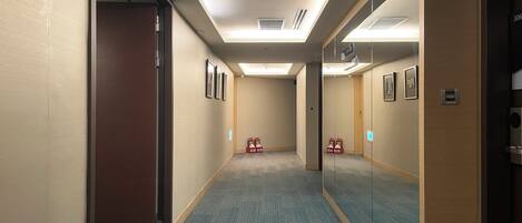 A hotel hallway with carpeted floors, framed pictures on the walls, and a door on the left.