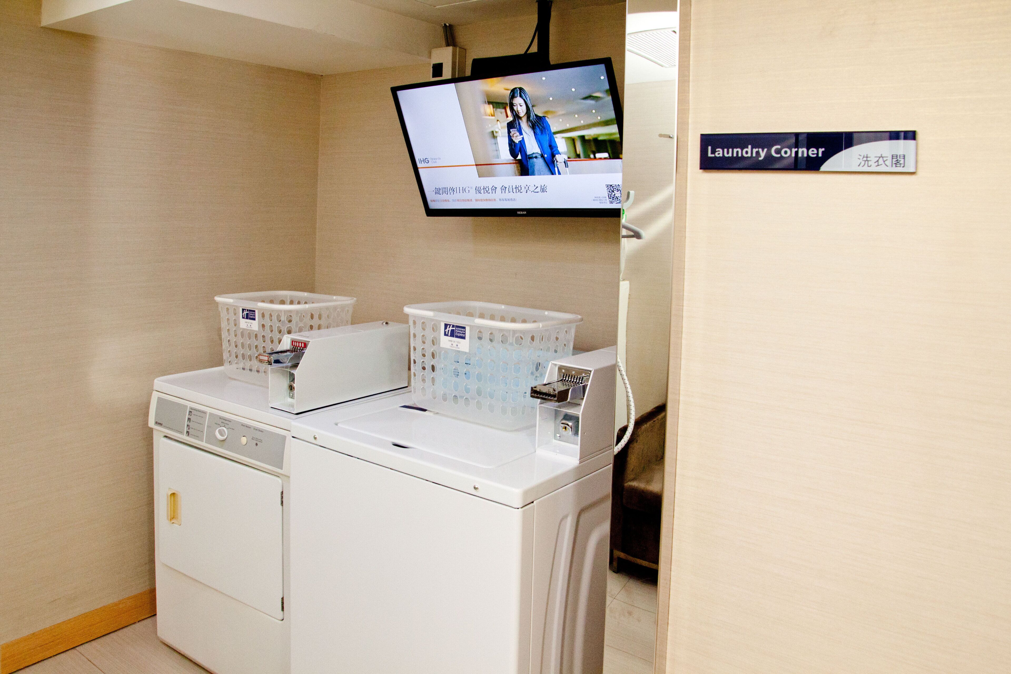 Un espace buanderie comprenant un lave-linge, deux paniers et un téléviseur fixé au mur.