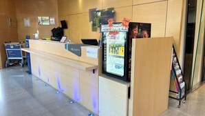 A hotel reception area with a counter, a refrigerator stocked with beverages, and a digital screen displaying information. - Holiday Inn Express Taoyuan by IHG (Taoyuan City)