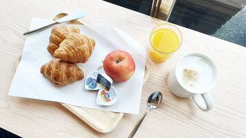 A breakfast tray with croissants, an apple, yogurt, a glass of orange juice, and a cup of coffee on a wooden table.
