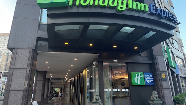 The exterior of a Holiday Inn Express hotel with a prominent green and white sign, large glass entrance, and a statue of a lion. - Holiday Inn Express Taoyuan by IHG (Taoyuan City)