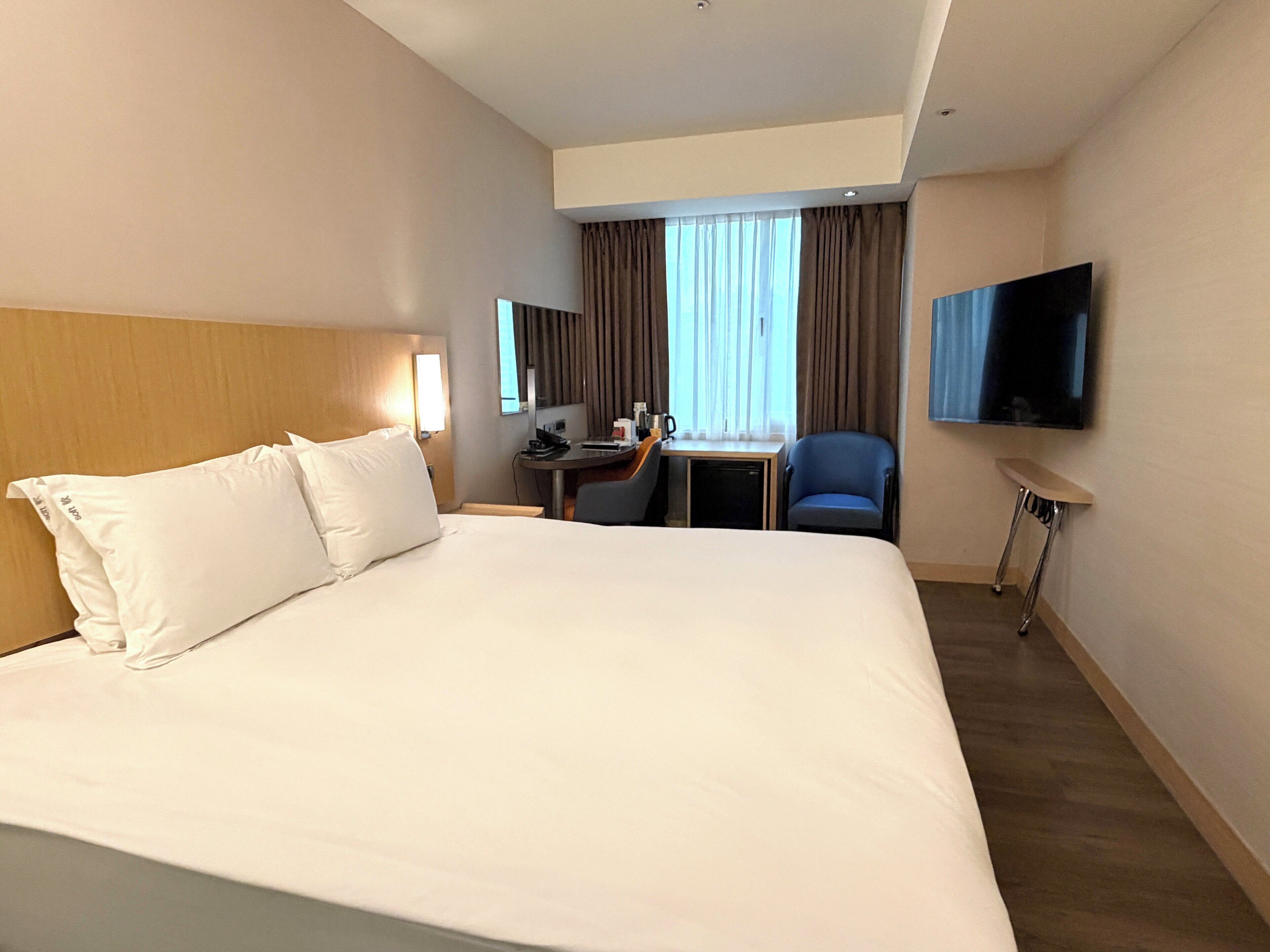 Habitación de hotel con una cama grande, un escritorio, una silla, un televisor y una ventana con cortinas.