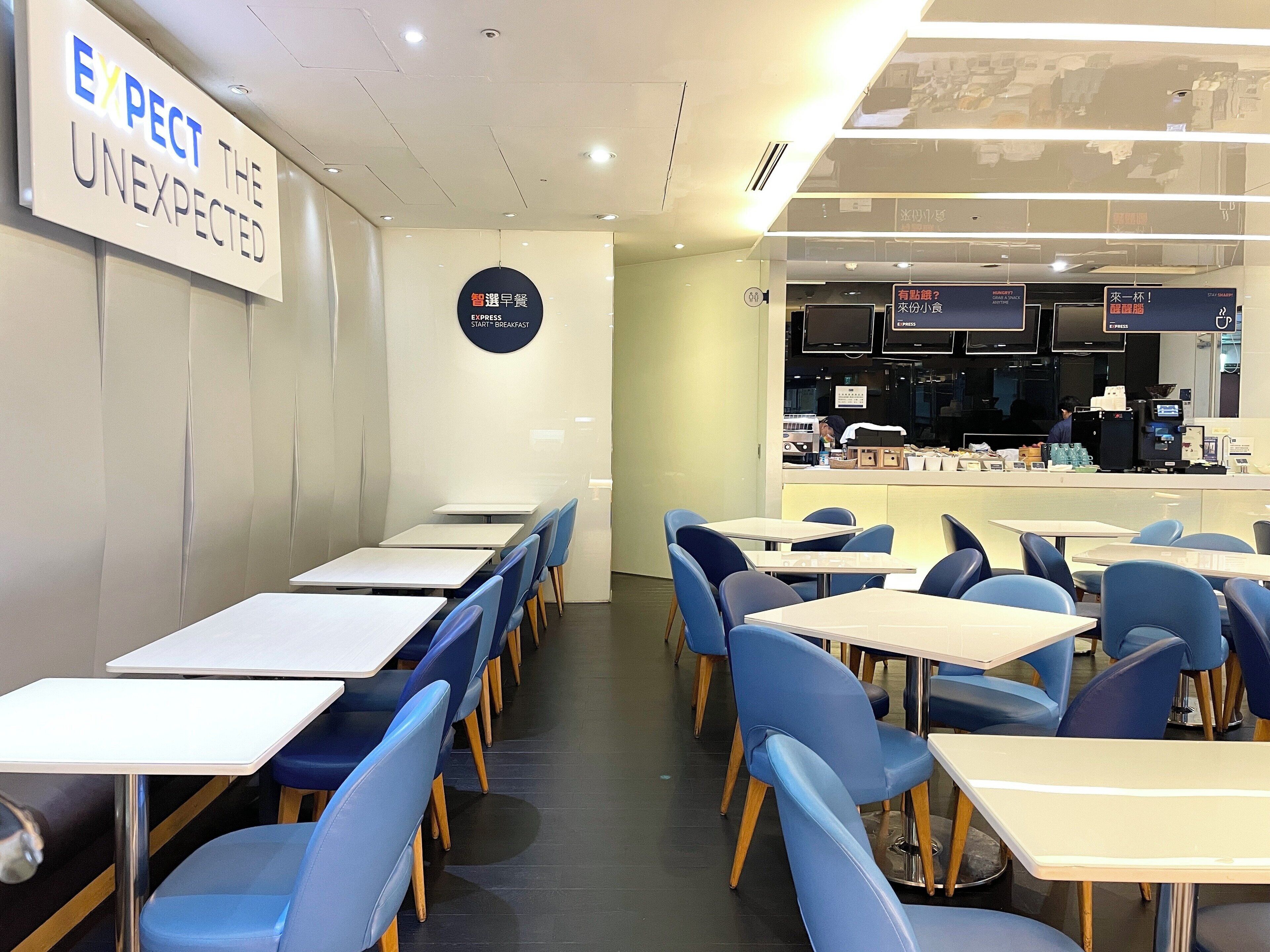A modern cafe with tables and chairs, a sign on the wall, and a counter area with a menu.