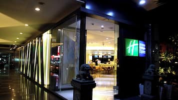 A modern hotel entrance with glass doors, a reception desk, and a digital signboard.