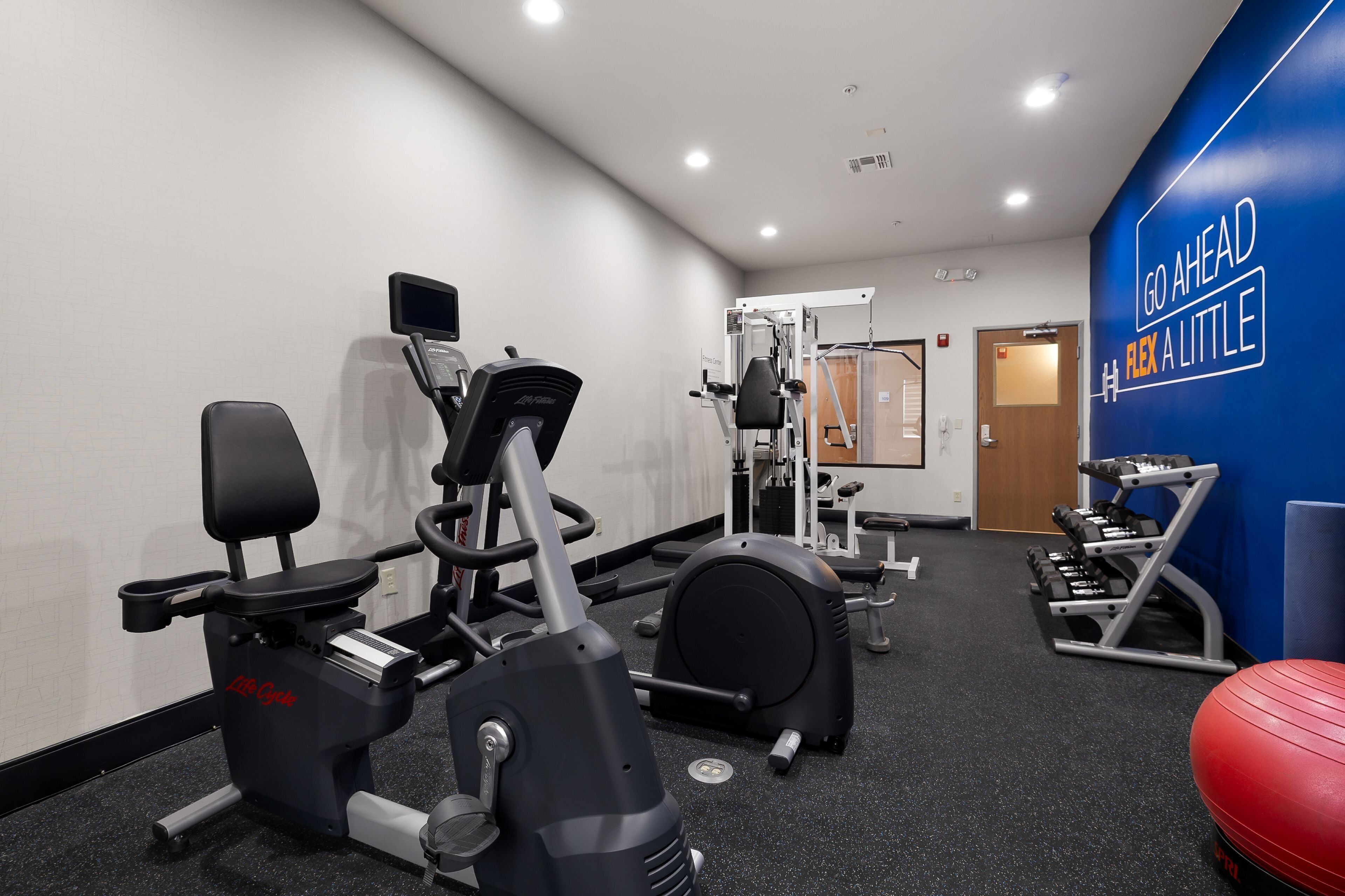 Un gimnasio con máquinas de cardio, equipo de levantamiento de pesas y una pared motivacional.