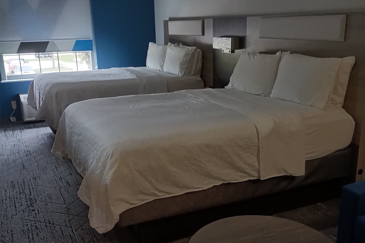 Habitació d'hotel amb dos llits, una taula rodona de fusta i vista a l'exterior per una finestra.