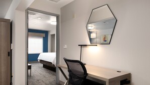 A hotel room with a wooden desk, a black office chair, a large mirror, and a bed with a blue accent wall.