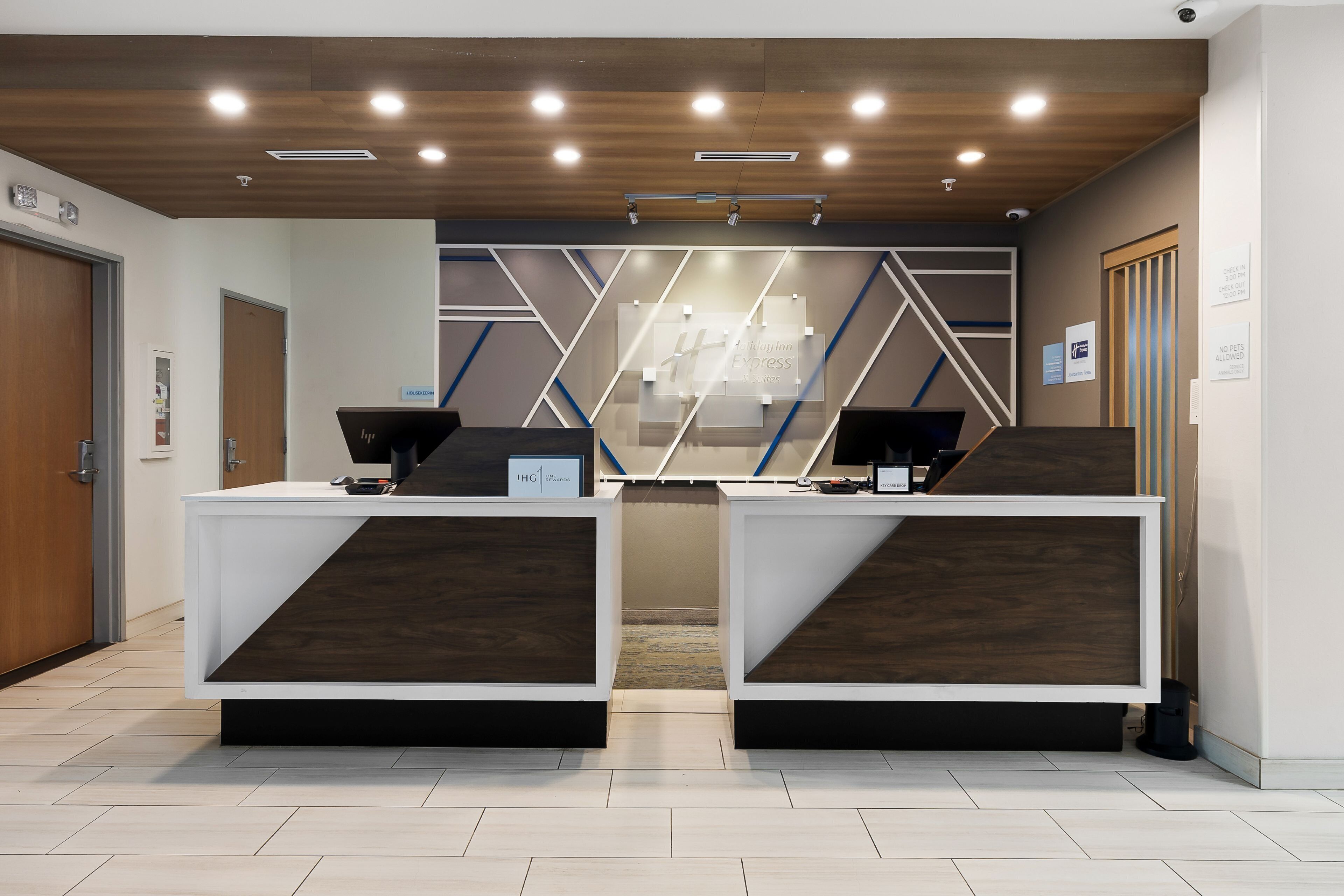A reception desk with two computer stations, wooden ceiling, and a geometric wall design.