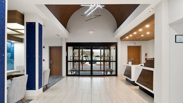 A modern hotel lobby with a central glass door entrance, a reception desk, and seating areas.
