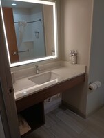 A bathroom with a white sink, a mirror with a light, and two bottles of Dove soap on the wall.