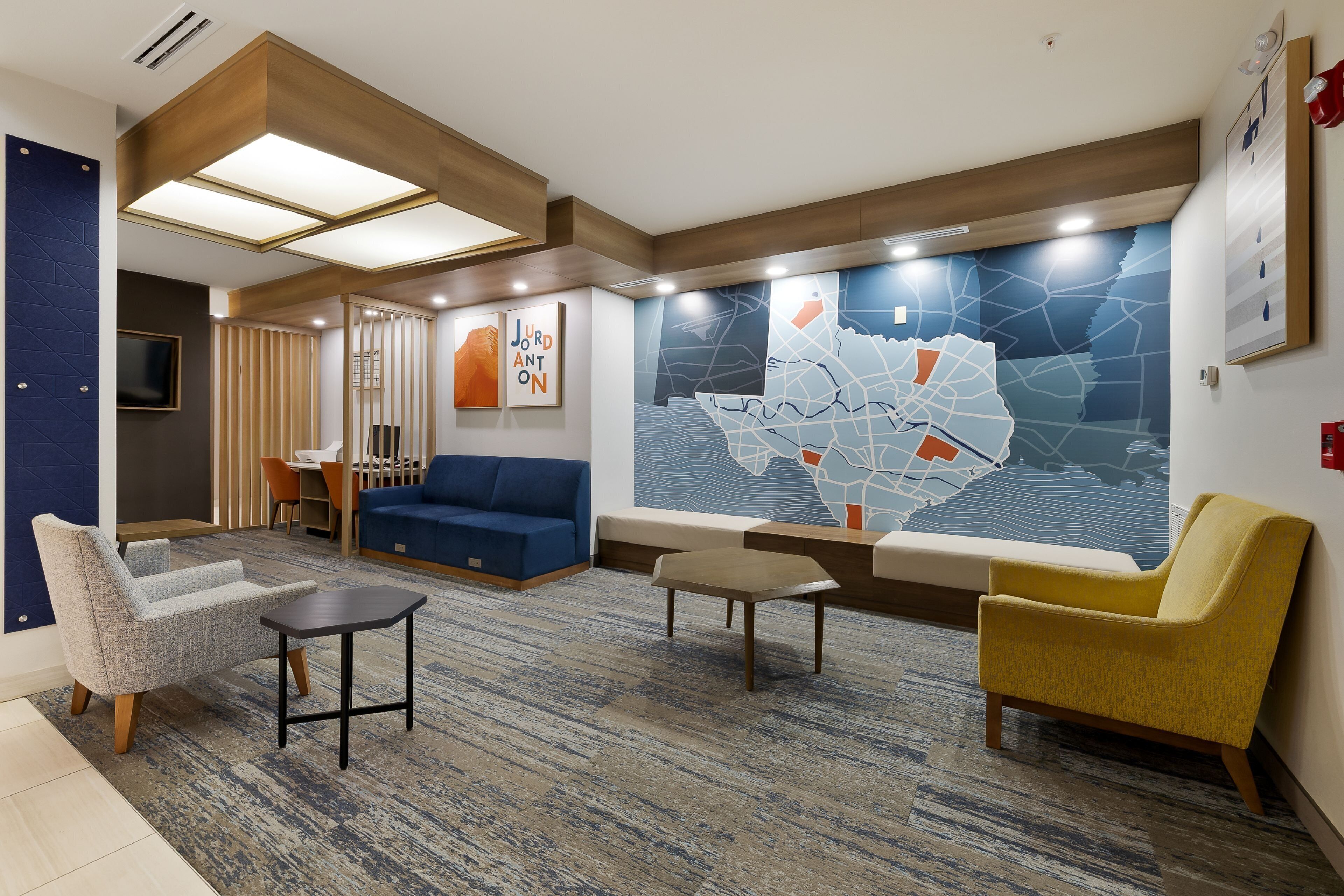 Un lobby moderno con un sofá azul, un sillón amarillo y una gran obra de arte abstracto en la pared.