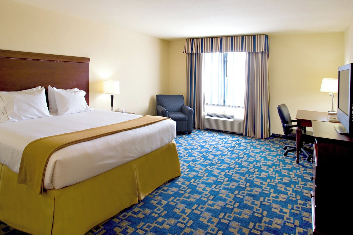 A hotel room with a large bed, a desk, a chair, and a television.