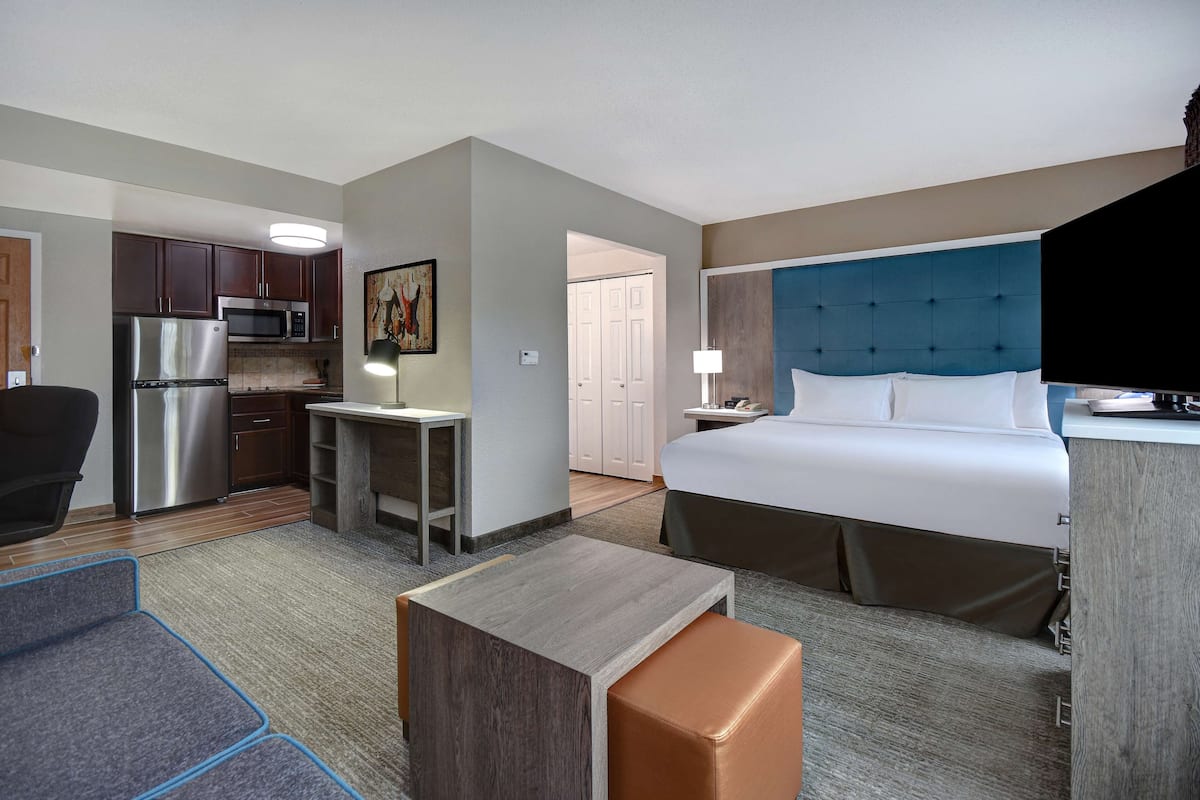 A hotel room with a bed, a desk, a refrigerator, a microwave, and a kitchenette.