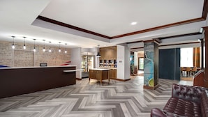 A hotel lobby with a herringbone patterned floor, a reception desk, a bar area, and a seating area with a leather sofa. - Homewood Suites by Hilton Yorktown Newport News (Yorktown)