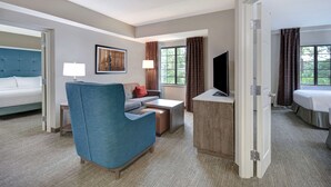 A hotel room with a bed, a sofa, a desk, a chair, a TV, and a window with curtains. - Homewood Suites by Hilton Yorktown Newport News (Yorktown)