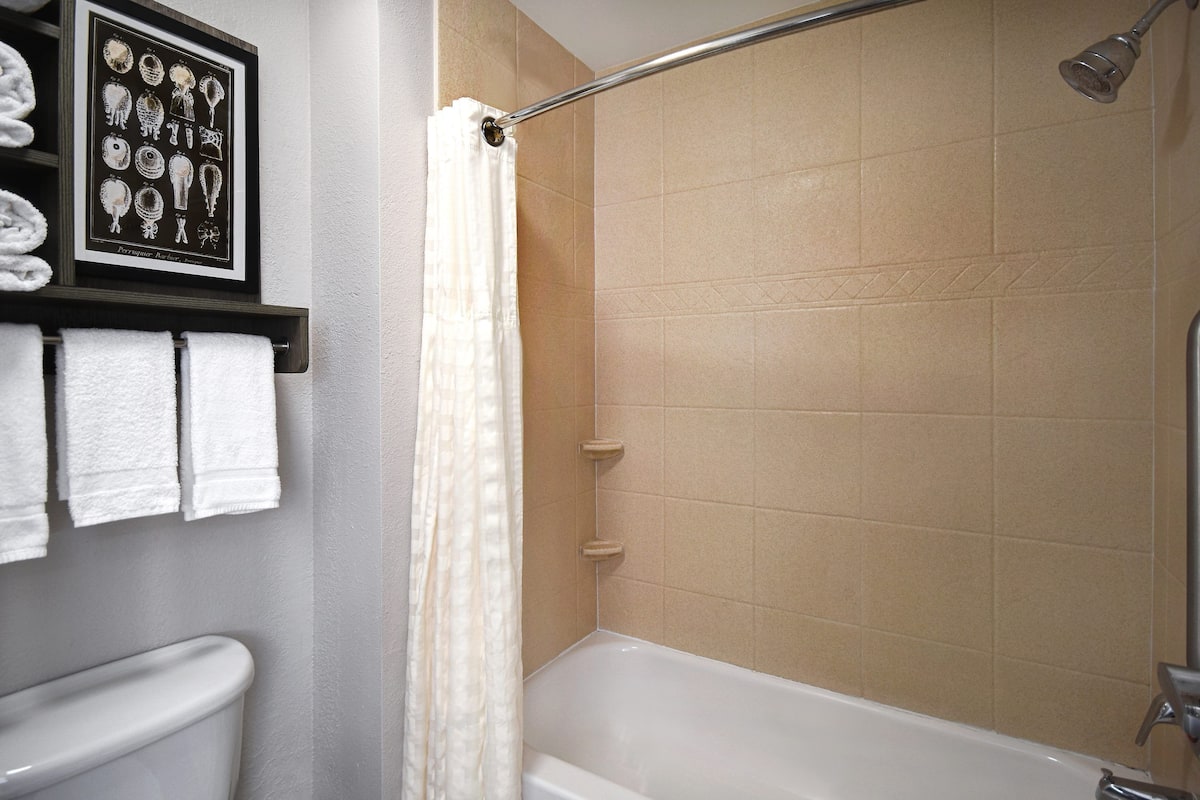 A bathroom with a bathtub, a shower, and a toilet. There is a framed picture on the wall and a towel rack with towels.