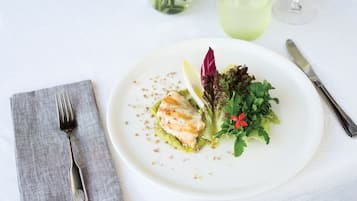 Un plato blanco con un trozo de pescado a la parrilla, vegetales verdes y una rodaja de limón sobre un mantel blanco.
